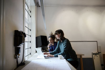 Female architects discussing over laptop at table in office