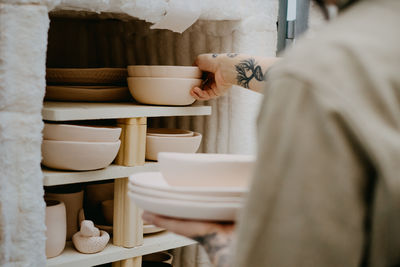 Unrecognizable crop artisan putting clay bowls and pots on shelf in creative studio