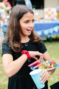 Tween girl smiles at a celebration while carrying a plate of fruit