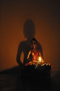 Illuminated lamp by buddha statue in darkroom