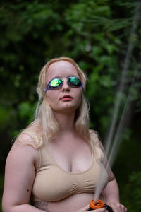 Portrait of young woman wearing sunglasses while standing in forest