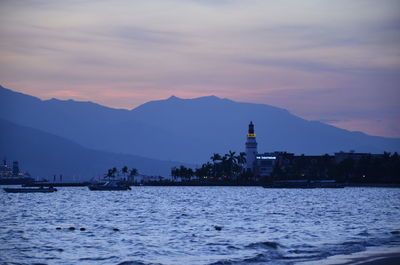 Sea by buildings against sky during sunset