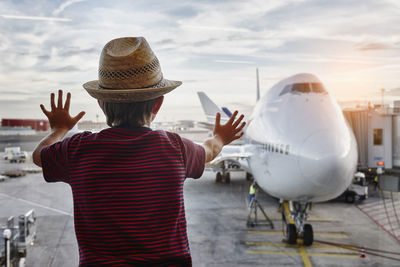 Boy wearing straw hat looking through window to airplane on the apron