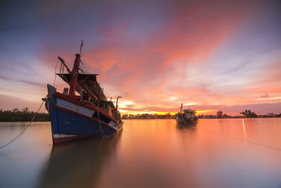 Fishing boats moored in sea against cloudy sky during sunset