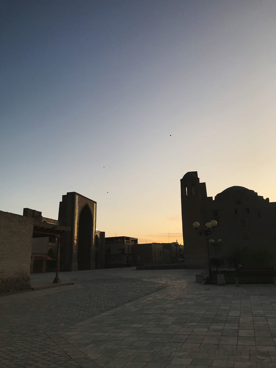 SILHOUETTE BUILDINGS BY STREET AGAINST SKY AT SUNSET