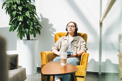 Young girl student in glasses using mobile phone, listen music in headphones in yellow chair 