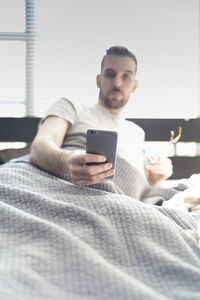 Young man using mobile phone while sitting on bed