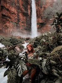 Portrait of woman standing amidst plants against waterfall