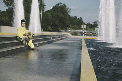 Full length of man in traditional clothing sitting on steps by fountain