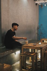 Side view of young man sitting on table