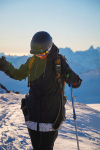 Adult girl on skis stands on a mountainside, admiring the mountain landscape, looking at the camera