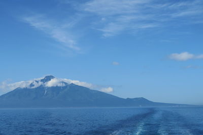 Scenic view of sea by mountains against blue sky