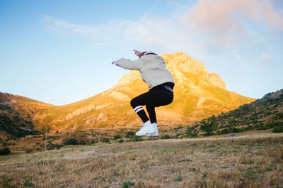 Back view of unrecognizable male in casual clothes jumping high against mountains