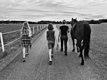Rear view of family with horse walking on dirt road against sky