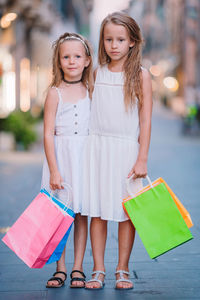 Portrait of young woman holding shopping bags while standing in city