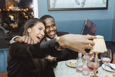 Young male and female friends taking selfie through smart phone at bar