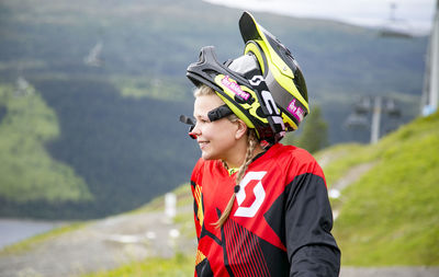 Young woman looking away while wearing crash helmet against mountain