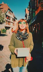 Portrait of young woman standing against building in city