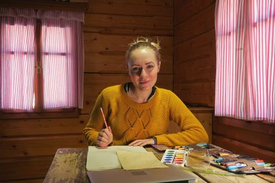 Portrait of young woman drawing on paper while sitting in cottage