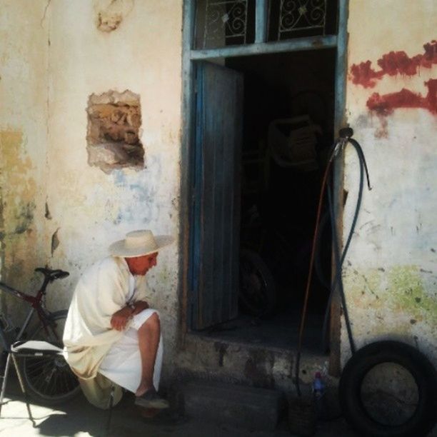 architecture, built structure, door, building exterior, wall - building feature, casual clothing, sitting, old, house, wall, full length, indoors, day, abandoned, window, lifestyles, side view, leaning