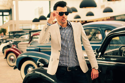 Young man wearing sunglasses standing by car