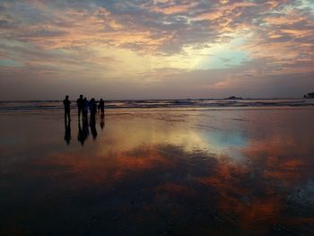 Silhouette people standing at beach against sky during sunset