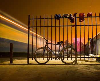 Bicycle parked on railing against sky at night