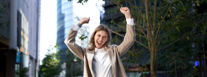 Side view of woman with arms raised standing against building