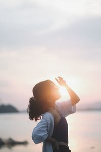 Side view of woman holding sea against sky during sunset