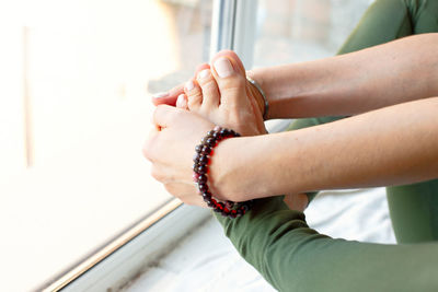 A slender woman in a green jumpsuit, in a yoga pose, clasped her feet in her arms