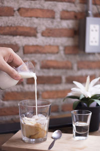 Cropped hand of person pouring milk in coffee on table