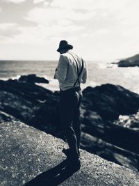 Rear view of a man standing at sea shore against sky