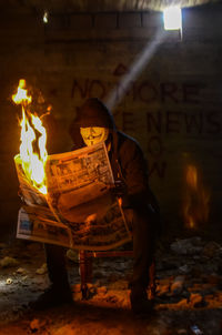 Man standing against illuminated fire at night