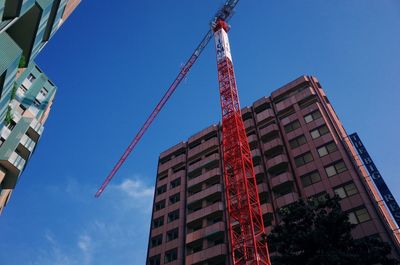 Low angle view of crane by building against blue sky