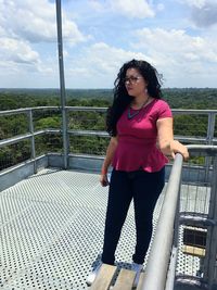 Young woman looking away while standing by railing against sky