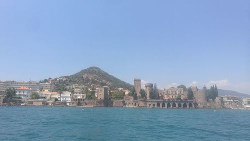 Sea by cityscape against clear blue sky