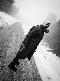 Side view portrait of man wearing gas mask while holding gun on road during winter