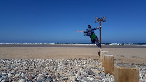 Rear view of man on wooden post at beach against clear sky