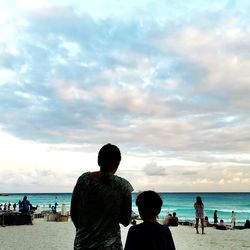 Rear view of people on beach against sky