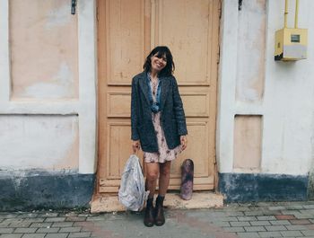 Smiling woman carrying backpack standing against closed door on sidewalk