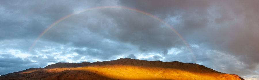 Rainbow over mountain against cloudy sky