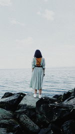 Rear view of woman looking at sea while standing on rock