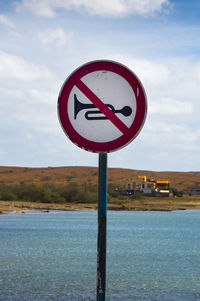 Close-up of road sign by lake against sky