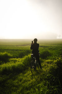 Rear view of woman standing on field taking picture against sky