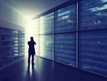 Rear view of silhouette man standing by window