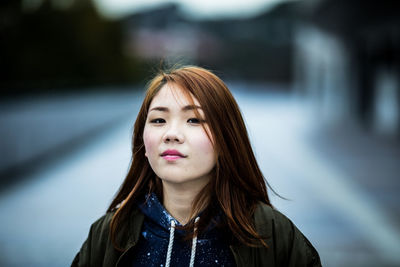 Portrait of young woman standing against blurred background