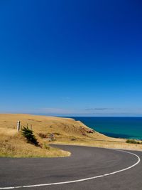 Road by sea against clear blue sky