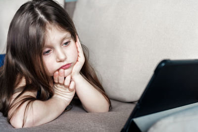 Cute girl watching video over digital tablet while lying on sofa at home