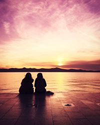 Silhouette couple sitting by sea against sky during sunset