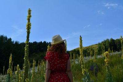 Rear view of woman standing by plants against sky